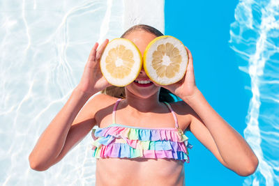 High angle view of girl holding fruits lying down by swimming pool