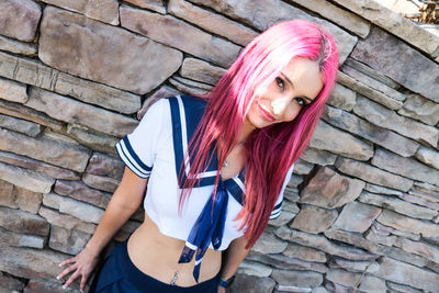 Portrait of beautiful young woman standing against brick wall