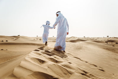 Rear view of people walking in desert against clear sky