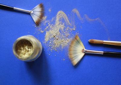 Directly above shot of make-up brushes with glitter on blue table