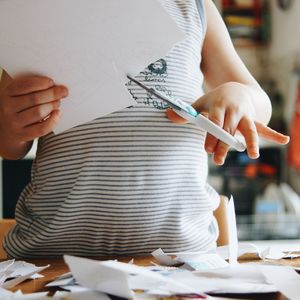 Midsection of child cutting papers on table while standing at home