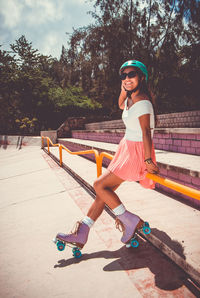 Full length of smiling young woman sitting on skateboard