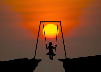 Rear view of silhouette boy on swing against sky during sunset