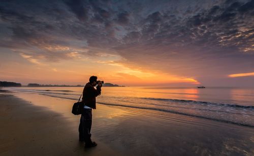 Man photographing at beach during sunset