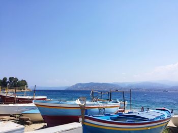 Boats moored on sea against clear blue sky