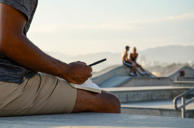 Midsection of man writing in diary while sitting outdoors