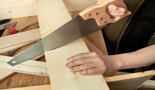 Close-up of craftsperson cutting wooden plank with hand saw