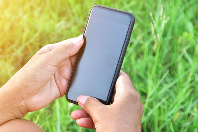 Cropped hands holding mobile phone on grassy field