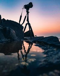 Reflection of silhouette rocks in sea against sky during sunset