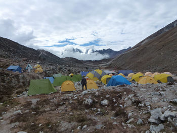 Rear view of man standing by tents at mountains against cloudy sky