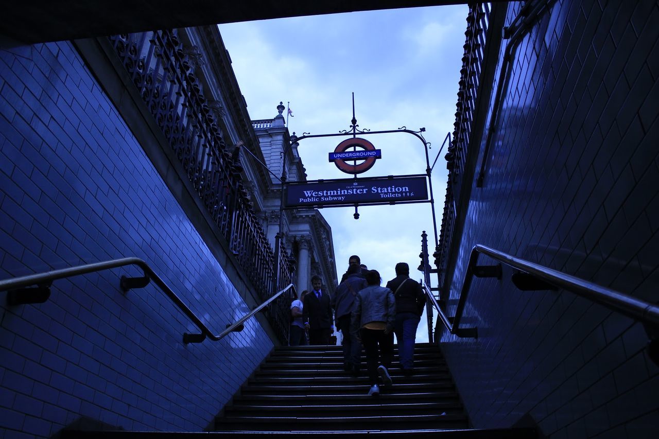 REAR VIEW OF PEOPLE WALKING ON STAIRCASE LEADING TOWARDS SKY