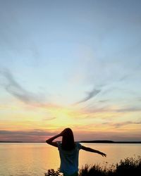 Rear view of woman standing at beach during sunset