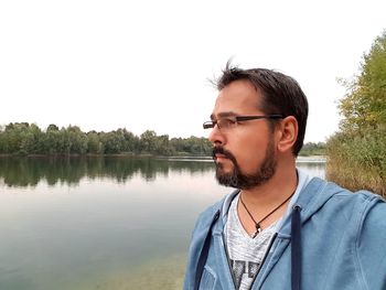 Young man standing by lake against clear sky