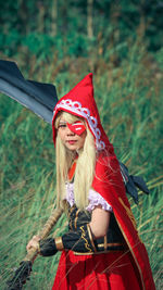 Portrait of young woman wearing red costume with sword while standing on field