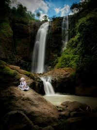 Teenage girl sitting by waterfall