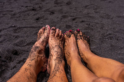 Closeup feet of a couple lying down on a black volcanic tropical beach - summer vacation concept