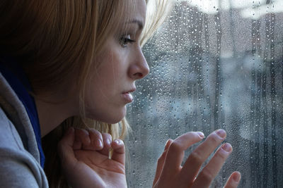 Close-up of young woman looking through wet window