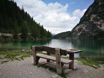 Empty bench at lakeshore in forest against cloudy sky