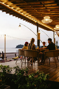 Family having food sitting on chairs at restaurant porch during vacation