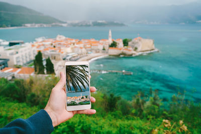 Midsection of person photographing sea against mountain