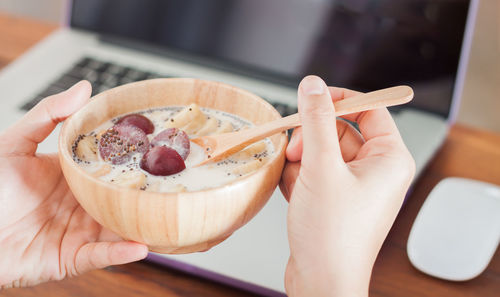 Close-up of hand holding bowl of milk and plum with chopped banana