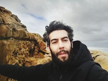 Portrait of young man on rock against sky