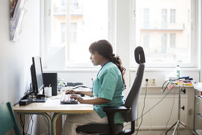 Side view of mature female doctor working over computer while sitting in clinic