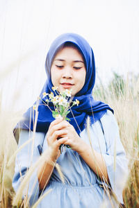 Portrait of beautiful young woman holding flower in field