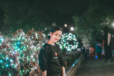 Young woman looking at illuminated christmas tree at night