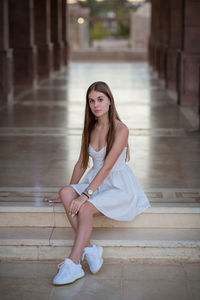 A young beautiful woman in white dress sits on a marble staircase