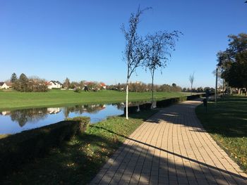 Footpath by lake against clear blue sky