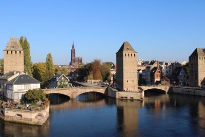 Bridge over river in city against clear blue sky