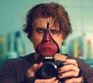 Reflection of man in mirror with halloween make-up while using camera