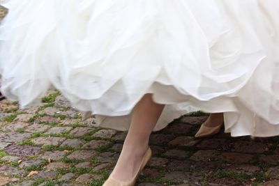 Low section of bride wearing wedding dress on footpath