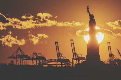 Silhouette statue against factory during sunset