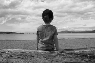 Rear view of boy on sea shore against sky