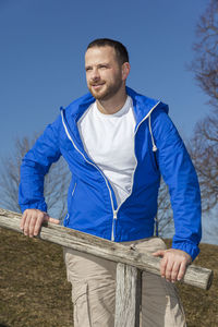 Man looking away while standing by railing against sky