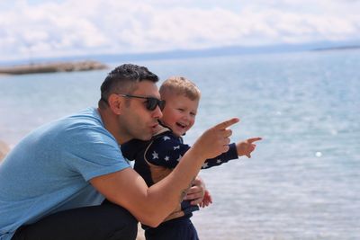 Father and son on sea shore against sky