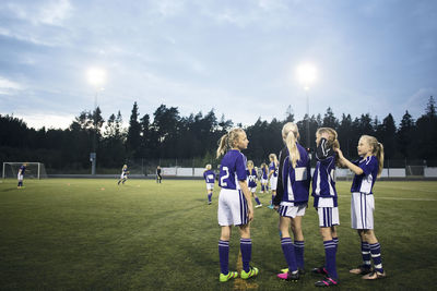 Girls standing on soccer field against sky