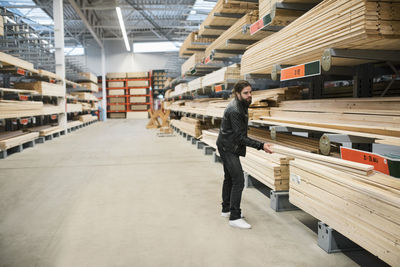 Side view of male customer holding wooden planks by shelves in hardware store