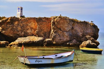 Boats moored at sea by rock formation against sky