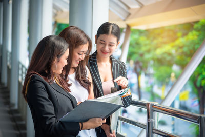 Colleagues discussing document while standing by railing in office