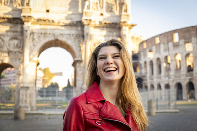 Young woman traveling to rome. woman smiling and posing fot a photo in front of the arch of titus.