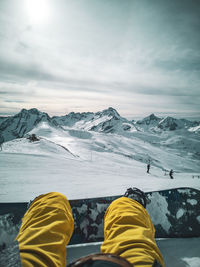 Low section of person on snowcapped mountains against sky