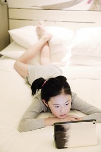 High angle view of girl using digital tablet while lying on bed at home