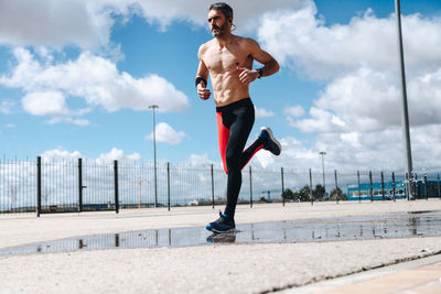 Full length of shirtless man looking at city against sky