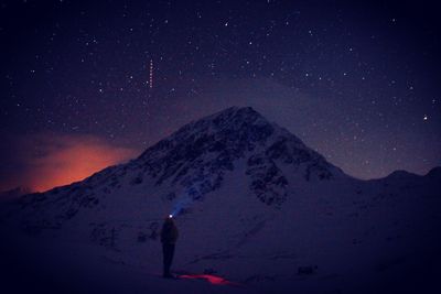 Silhouette woman standing by snowcapped mountain against sky at night