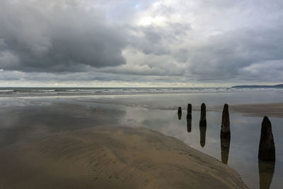 Wooden posts on beach against sky