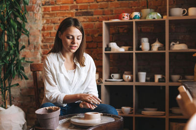 Young attractive woman in white shirt ceramic artist working on potter's wheel in the studio