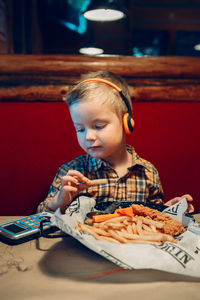 Boy eating food while playing video game at table in restaurant